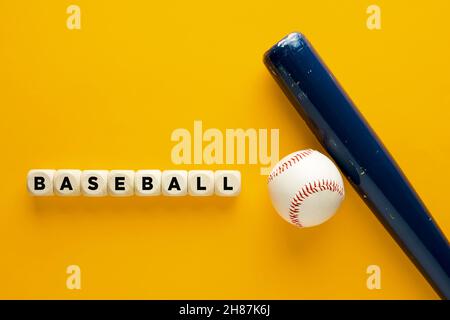 Baseballball und blauer Holzschläger auf gelbem Hintergrund mit dem Wort Baseballspiel auf Holzwürfeln. Stockfoto