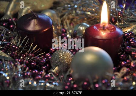 Adventkonzept Weihnachtslicht mit Kerzen Kugelkugel Sterne.Studioaufnahme eines schönen Adventkranzes mit Kugeln und brennender lilafarbener Kerze Stockfoto