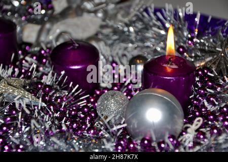 Weihnachtskranz im Adventkonzept Weihnachtslicht mit Kerzen Kugel-Kugel-Sterne.Silber und violett Adventskranz mit Kugeln und brennende lila Kerze Stockfoto