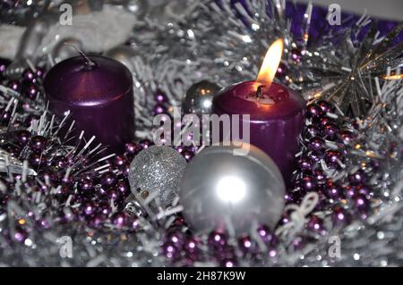 Erster sonntag im Adventkonzept Weihnachtslicht mit Kerzen Kugelkugel Sterne.Studioaufnahme eines schönen Adventkranzes mit Kugeln und brennender lilafarbener Kerze Stockfoto