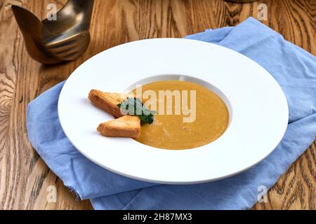 Kürbiscremesuppe mit Croutons auf blauer Serviette auf Holzhintergrund Stockfoto