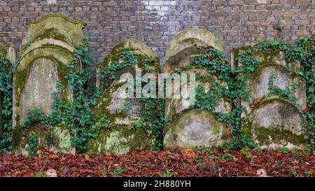 Uralt bewachsen mit Moos und Efeu Pflanzen Grabsteine und Gräber auf dem Kirchhof Garten am Herbstmorgen. Stockfoto