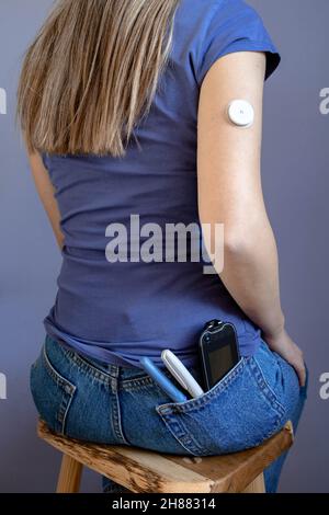 Mädchen sitzt mit Flash Glucose Monitor, Patch auf ihre Hand und Monitor in ihrer Tasche Stockfoto