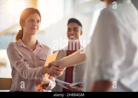 Eine Gruppe junger Geschäftsleute schüttelt die Hände, als sie sich in einer freundlichen Atmosphäre auf dem Flur trafen. Unternehmen, Mitarbeiter, Unternehmen Stockfoto