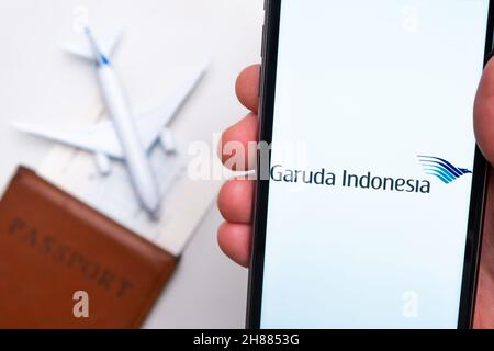 Die Anwendung Garuda Indonesia Airline wird auf dem Smartphone-Bildschirm angezeigt. Im Hintergrund befinden sich ein verschwommenes Flugzeug, ein Reisepass und eine Bordkarte. November 2021, San Francisco, USA Stockfoto