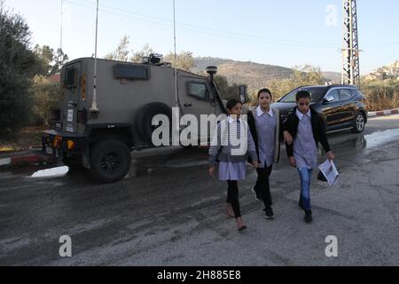 Westufer, Nablus, Palästina. 28th. November 2021. Palästinensische Studenten kommen an israelischen Soldaten vorbei, nachdem die Straße, die zu den Schulen führt, von israelischen Siedlern im Dorf al-Lubban al-Sharqiya, südlich der Stadt Nablus im Westjordanland, gesperrt wurde. Kredit: Nasser Ishtayeh/ZUMA Wire/Alamy Live Nachrichten Stockfoto