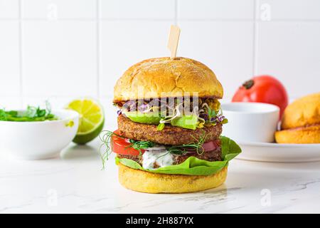 Kochen veganer Burger mit Avocado, Tomaten- und Nusssoße, weißer Fliesenhintergrund mit Zutaten. Stockfoto