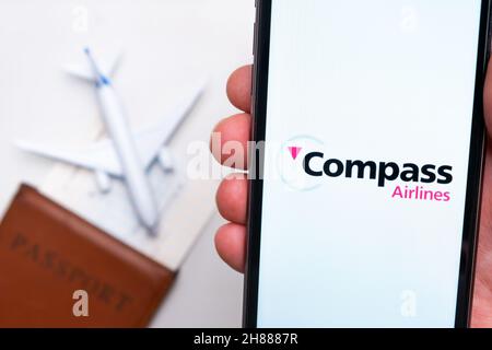 Compass Airlines App-Logo auf dem Bildschirm des Mobiltelefons. Ein verschwommenes Bild eines Flugzeugs, eines Passes und einer Bordkarte im Hintergrund. November 2021, San Francisco, USA Stockfoto