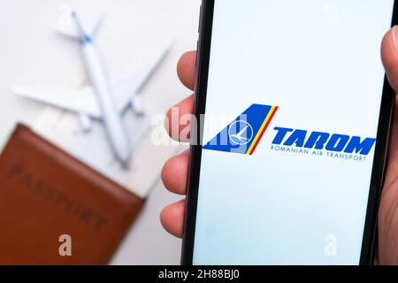 Tarom Rumänische Air Transport Airlines App auf dem Handy-Bildschirm in mans Hand mit Flugzeug, Bordkarte und Reisepass im Hintergrund. Das Konzept der mobilen Anwendung der Fluggesellschaften. November 2021, San Francisco, USA Stockfoto