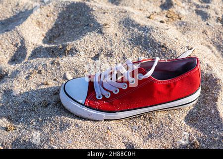 Ein roter Sneakerschuh im Hintergrund des Sandstrandes Stockfoto