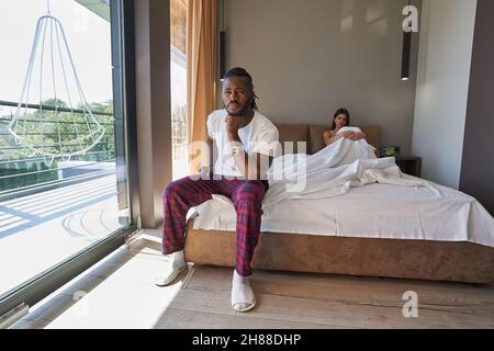 Trauriges junges gemischtes Paar, das im Schlafzimmer saß Stockfoto