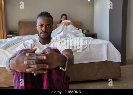 Gelaunter junger Mann und Frau, die im Schlafzimmer auseinander sitzen Stockfoto