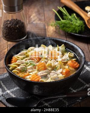 Dampfaufsatz mit Hühnernudelsuppe mit Karotten und Dill auf einem rustikalen Holztisch Stockfoto