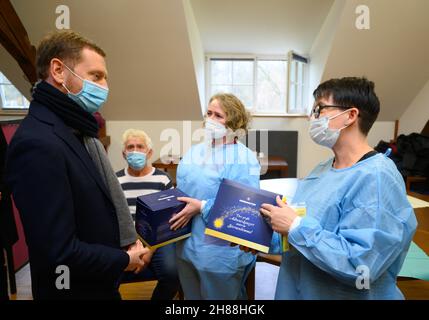 28. November 2021, Sachsen, Schmochtitz: Michael Kretschmer (CDU, l), Ministerpräsident von Sachsen, überreicht Herrnhuter Stars als Dankeschön an zwei Frauen, die im Rahmen einer Impfkampagne im Bildungsgebiet Sankt Benno bei Bautzen Menschen gegen das Coronavirus impfen. Mit einer einmal-Impfkampagne in Kooperation mit dem Deutschen Roten Kreuz (DRK) am 1. Advent wollen die sächsischen Kirchen Ärzte und mobile Teams dabei unterstützen, die Bevölkerung gegen Covid-19 zu impfen. Foto: Robert Michael/dpa-Zentralbild/dpa Stockfoto