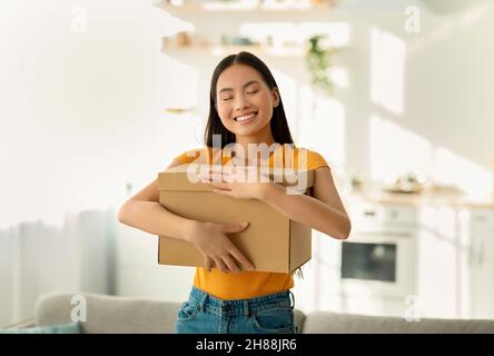 Überglücklich asiatische Dame umarmt Karton Paket, Erhalt lang erwartete Lieferung, immer online bestellen, zu Hause stehen Stockfoto