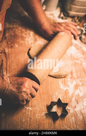 Lebkuchen backen, Teig auf Holztisch Rollen. Ältere Frau, die in der heimischen Küche mit Nudelholz arbeitet. Getöntes Bild Stockfoto