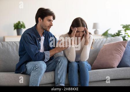 Junge kaukasische Paar sitzen auf dem Sofa, Ehemann beruhigt verärgert Frau zu Hause innen Stockfoto