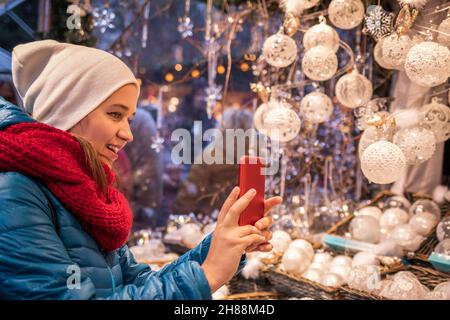 Frau fotografiert weihnachtsdekoration auf ihrem Smartphone. Tourist auf dem weihnachtsmarkt in Wien, Österreich. Erinnerungen aus dem Urlaub in Europa Stockfoto
