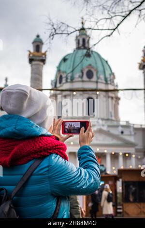 Tourist, der während der weihnachtsfeiertage mit ihrem Smartphone die St. Charles Chirche, Karlskirche, Karlsplatz in Wien fotografiert. Reiseerinnerungen Stockfoto