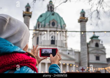 Tourist, der während der weihnachtsfeiertage mit ihrem Smartphone die St. Charles Chirche, Karlskirche, Karlsplatz in Wien fotografiert. Reiseerinnerungen Stockfoto