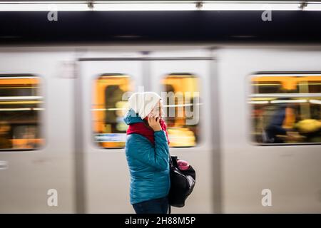 Frau, die in der U-Bahn-Station steht und telefoniert. Die U-Bahn fährt in unscharfer Bewegung. Öffentliche Verkehrsmittel in der Stadt Stockfoto