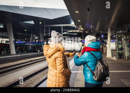 Zwei Frauen warten am Bahnhof auf den Zug und überprüfen die Zeit. Zug verzögern. Transport- und Reisekonzept Stockfoto