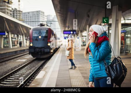 Fahrgäste am Bahnhof Rairoad und ankommendem Zug. Frau, die vor der Reise ein Smartphone benutzt. Öffentliche Verkehrsmittel in der Stadt Stockfoto