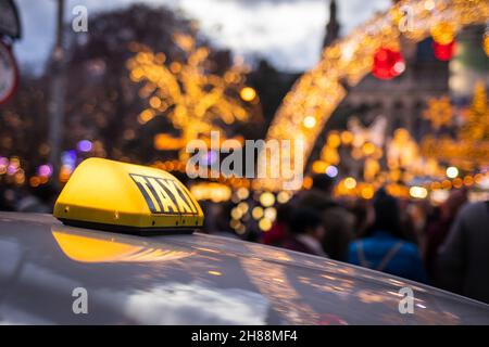 Taxi-Auto auf der Stadtstraße in der Nähe des Weihnachtsmarktes am Rathausplatz, Wien, Österreich. Gelbes Taxistand auf dem Dach des Autos bei Nacht. Öffentliche Verkehrsmittel Stockfoto