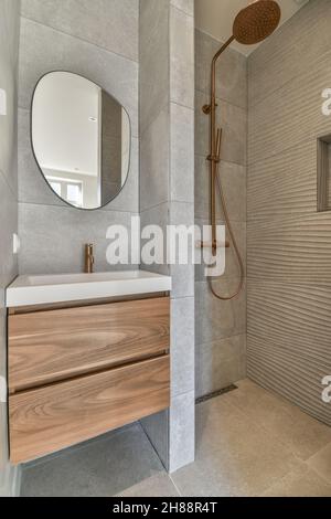 Stilvolles Waschbecken mit großem runden Spiegel und begehbarer Dusche in der Nähe Stockfoto