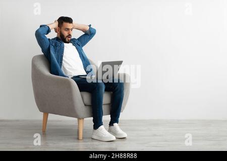 Erschrockener arabischer Freiberufler, der auf den Laptop-Bildschirm schaut, den Kopf ergreifend, Fehler im Geschäftsprojekt macht, den Termin verpasst Stockfoto