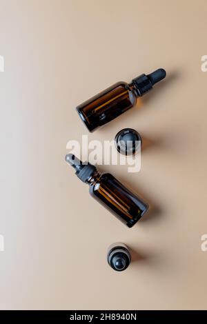 Weiße, braune Flaschen aus ätherischem Öl mit Pipette auf beigem Hintergrund, Draufsicht. Hautpflegekonzept mit Naturkosmetik. Stockfoto