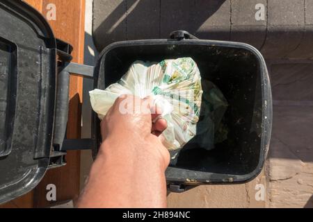 Erwachsene Männer, die einen biologisch abbaubaren Beutel mit Lebensmittelabfällen in einen Futtermittelbehälter fallen lassen Stockfoto