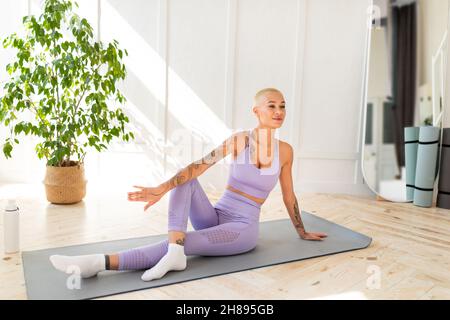 Friedliche Frau, die in Yoga-Pose sitzt und lächelt, auf einer Trainingsmatte im Wohnzimmer trainiert, freier Platz Stockfoto