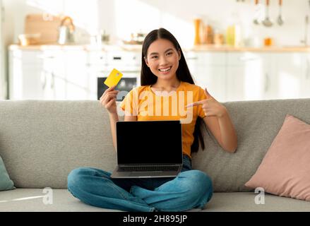 Ferneinkaufskonzept. Glückliche asiatische Frau mit Kreditkarte und Laptop Kauf im Web, mockup Stockfoto