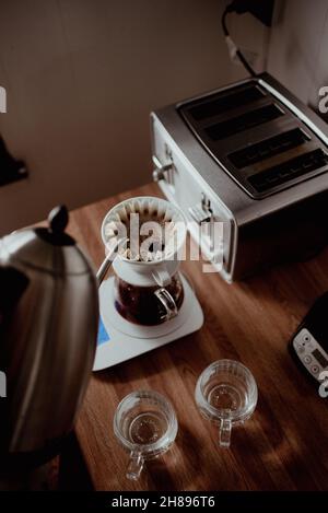 Heißes Wasser aus dem Schwanenhals-Wasserkocher in die Kaffeemaschine gießen, langsam Kaffee extrahieren, frisch gebrühten gefilterten Kaffee, Kaffee zu Hause zubereiten Stockfoto