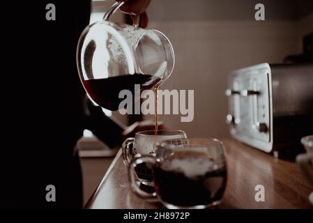 Der junge, tausendjährige Hipster-Mischling gießt frisch gemahlenen und gebrühten Kaffee in seiner Küche zu Hause in Glas-Becher Stockfoto