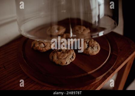 Heben Sie das Glas-Gebäck-Display an, um frisch gebackene hausgemachte Salzschokolade-Chip-Cookies zu zeigen. Moody Hipster, natürliche Beleuchtung auf Keksen, Gebäck Stockfoto