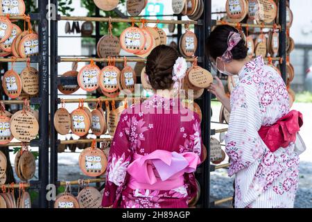 Junge japanische Frauen in traditionellem Kimono-Kostüm lesen Maneki Neko oder winken Glückskatze-ema-Gebetstafeln am Imado Jinja-Schrein, einem schintoistischen Schrein, der sich in Asakusa, Tokio, Japan, der Liebe widmet. Die Gläubigen hängen die Tafeln mit ihren Wünschen, Träumen oder Gebeten im Tempel auf. Stockfoto