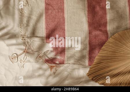 Gestreiftes Strandtuch aus Leinen mit Fransen, leere Cocktailgläser und getrocknetes Palmblatt am Sandstrand mit Schatten von Palmen. Entspannung und tropisch Stockfoto