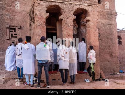 Lalibela, Äthiopien - 23. Mai 2021: Gemeindemitglieder, die von außerhalb einer Kirche an einer Messe teilnehmen und weiße Kleidung über ihren üblichen Kleidern tragen Stockfoto