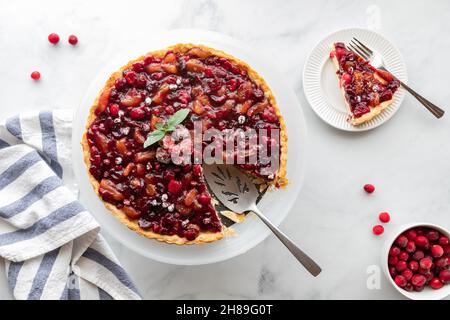 Draufsicht auf eine Cranberry-Tarte mit einer Scheibe auf einem Teller. Stockfoto
