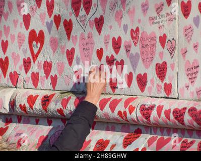 London, Großbritannien. 28th. November 2021. Ein Besucher fügt der National COVID Memorial Wall vor dem St. Thomas' Hospital einen Namen hinzu. Mehr als 150.000 rote Herzen wurden von Freiwilligen und Mitgliedern der Öffentlichkeit gemalt, eines für jedes Leben, das in Großbritannien bisher durch Coronavirus verloren ging. Kredit: SOPA Images Limited/Alamy Live Nachrichten Stockfoto