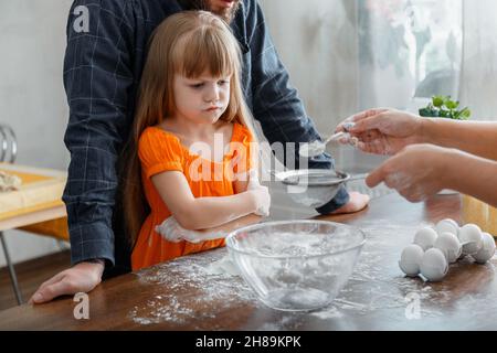 Missgunst von Kindern. Emotionales Porträt von kleinen verärgerten Kind Mädchen beim Backen Kochen Abendessen mit der Familie in der Küche zu Hause Interieur. Echt Stockfoto