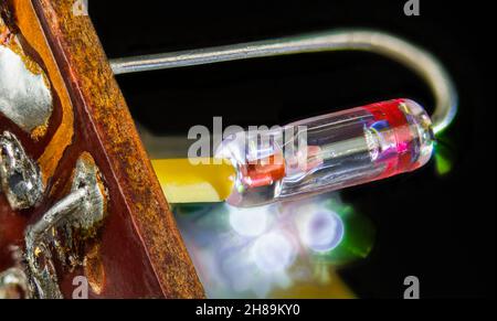 Vintage-Halbleiter-Germaniumdiode mit Kristalldetektor im geschweißten Glasrohr. Nahaufnahme eines in der Leiterplatte gelöteten elektrischen Retro-Bauteils. Stockfoto