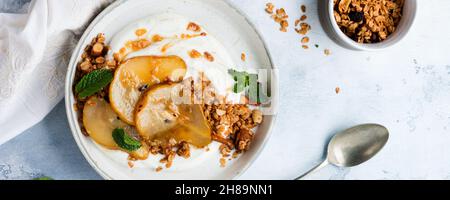 Griechischer Joghurt mit karamellisierter Birne, Müsli, Nüssen und geschmolzenem Zucker für ein gesundes Frühstück auf einer grauen Keramikplatte. Rustikaler Stil. Draufsicht. Stockfoto