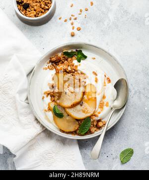 Griechischer Joghurt mit karamellisierter Birne, Müsli, Nüssen und geschmolzenem Zucker für ein gesundes Frühstück auf einer grauen Keramikplatte. Rustikaler Stil. Draufsicht. Stockfoto