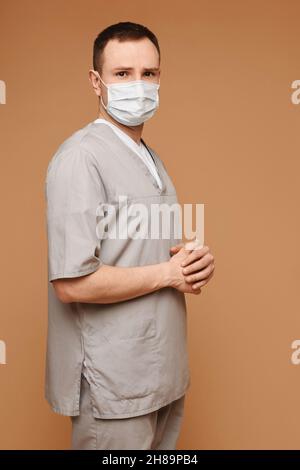 Gesundheitsarbeiter, Medizin, Covid-19 und pandemisches Selbstquarantänekonzept. Hübscher Arzt, eine Krankenschwester in grünen Peelings auf dem beigen Hintergrund. Stockfoto