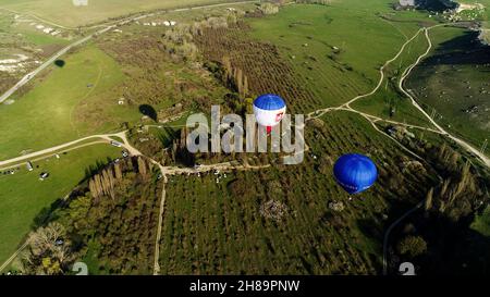 Luftaufnahme von bunten Luftballons am Himmel über der Landschaft, Frankreich. Aufnahme. Fliegen über Bäumen, Büschen, grünen Feldern und Parkautos Stockfoto