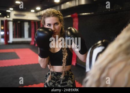 Zwei junge Frauen in Boxhandschuhen führen Sparring durch, Blick von der Seite eines der Athleten. Frauen Fitness-Boxen Training im Fitnessstudio Stockfoto