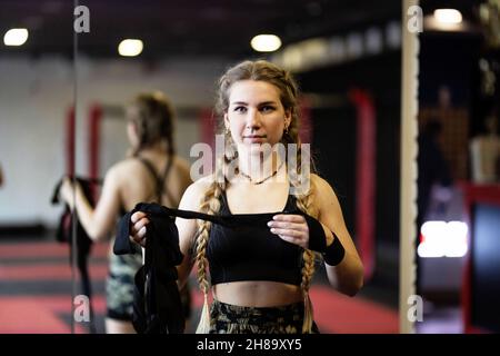 Eine junge Frau mit Zöpfen bereitet sich auf ein Training vor, sie wickelt einen engen Verband um ihre Hände, um sie zu schützen.das Fitness-Boxen-Workout der Frauen im Fitnessstudio Stockfoto